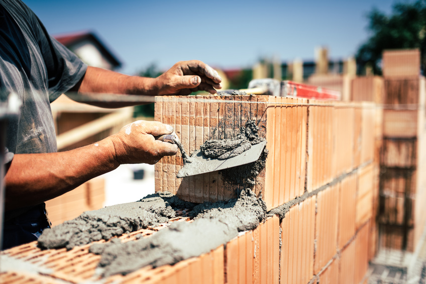 Industrial construction worker using spatula and trowel for building walls with bricks and mortar